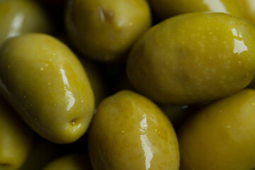 Green marinated olives in a bowl,
 horizontal background macro shot. Beautiful organic olives on dark wooden table, close up textured view, copy space.