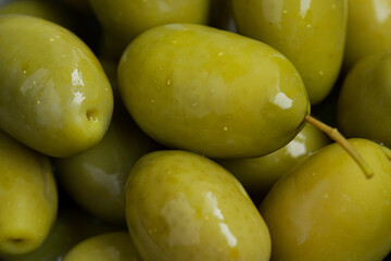 Green marinated olives in a bowl,
 horizontal background macro shot. Beautiful organic olives on dark wooden table, close up textured view, copy space.