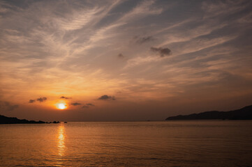 Fototapeta na wymiar Beautiful seascape at sunset. Sun setting behind a mountain and sea with calm water movement.