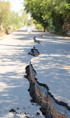 Asphalt road collapsed with cracks in sunny day. Vertical view. 