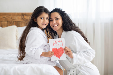 Cheerful little girl with gift card hugging her mom