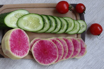 Red Chinese radish and green cucumber, cut into slices on a plastic board.