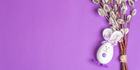 Sprig of willow isolated on lilac background with handmade funny bunny from the egg