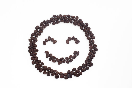 Roasted coffee beans arranged in a smiling face on a white background.