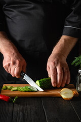 Chef cutting a green cucumber in kitchen in the restaurant. Making delicious salad with fresh vegetables