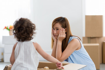 Happy small Asian family while moving into new home. Young Asian mother and her little toddler girl playing together while moving into new home with cardboard boxes on background