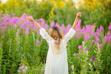 The girl stands with her back raised her hand with a bouquet of flowers on a background of greenery