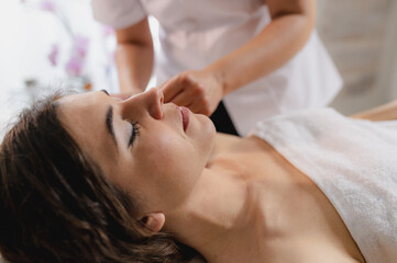 Woman lying on spa bed and beautician doing relaxing head massages.