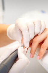 Manicure master applying electric nail file machine removing old nail polish on fingernails in a nail salon