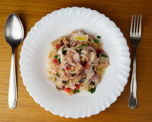 Delicious Peruvian hake and tune ceviche with vegetables, spices and lime in a white dish with cutlery. Top View