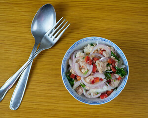 Delicious Peruvian hake and tune ceviche with vegetables, spices and lime in a ceramic bowl with cutlery. Top View