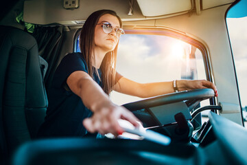 Portrait of beautiful young woman professional truck driver sitting and driving big truck. She is...