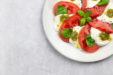 Traditional italian caprese salad with sliced tomatoes, mozzarella, basil, pesto sauce and spice on a light background. Top view. Copy space. Close up.
