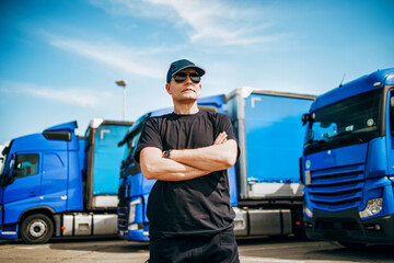 Professional truck driver with hat and sunglasses confidently standing in front of big and modern...