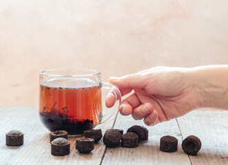A hand holding a cup of traditional Chinese puer tea with aged puerh tea bricks on wooden...
