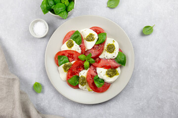 Traditional italian caprese salad with sliced tomatoes, mozzarella, basil, pesto sauce and spice on a light background. Top view.