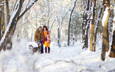 Fototapeta na wymiar Young couple smiling and having fun in winter park with their husky dog