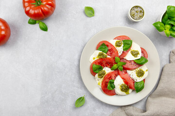 Traditional italian caprese salad with sliced tomatoes, mozzarella, basil, pesto sauce and spice on a light background. Top view. Copy space.