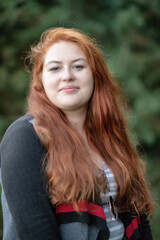 Fototapeta premium Portrait of a young beautiful red-haired plump girl in the forest.