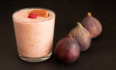 A glass cup of yogurt, with raspberries on top. Next to three pieces of figs. Selective focus.