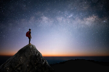 Silhouette of young traveler and backpacker standing on the rock watched the star and milky way. He...