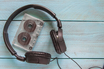 Black headphones and a transparent audio tape lie on a blue wooden background. Top view
