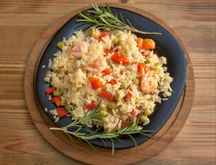 Rice with shrimp and vegetables, risotto, pilaf on a black plate, wooden background