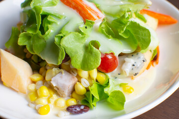 Salad with fruit and fresh vegetable topped with salad dressing in a white dish on wooden table