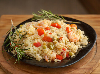 Rice with shrimp and vegetables, risotto, pilaf on a black plate, wooden background