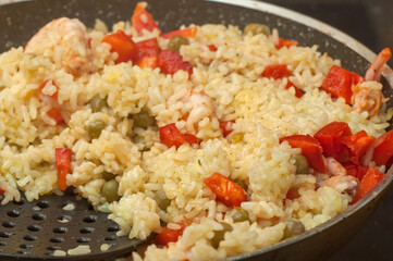 Rice with shrimp and vegetables, risotto, pilaf in a black pan, wooden background. to interfere