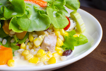 Salad with fruit and fresh vegetable topped with salad dressing in a white dish on wooden table