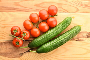 Several green cucumbers and red ripe, cocktail tomatoes on a twig, close-up, on a wooden table, top view.