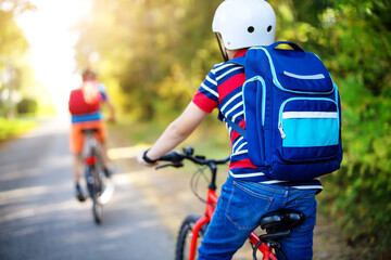 Children with rucksacks riding on bikes in the park near school.