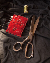 Sewing vintage scissor, clips on red pillow, thread roll line on black background - sewing equipment with space to text