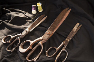 Many scissors for sewing and thread roll line on black textile background - sewing equipment with space to text - sustainable method
