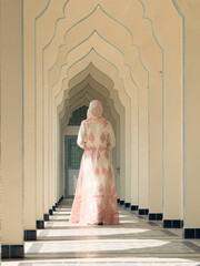 Rear view of young Muslim woman wearing beautiful traditional clothing, walking in the walkway. Vertical image.
