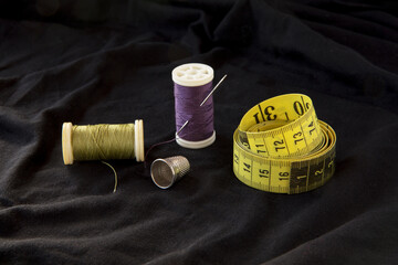 Sewing measure ruler, needle, thread roll lines and thimble on black textile background - sewing accessories with space to text