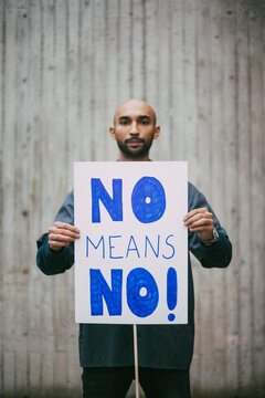 Portrait of male activist holding no means no poster against against wall