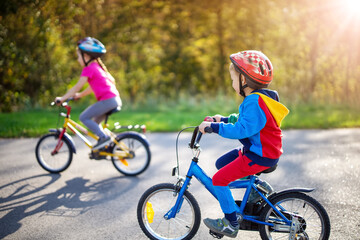 Cute children riding on bicycles on asphalt road in summer.