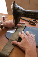 Man's hands behind sewing machine with watch. Sew workshop. textile vintage sewing at home on wood table, sustainable sewing