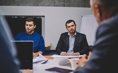 Confident male colleagues in formal clothes briefing on strategy discussing together exchange during working time, successful business persons analyzing investment experience during brainstorming