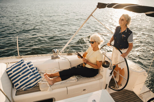 Senior woman sailing boat while female friend using digital tablet