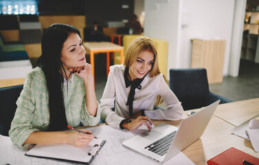 Caucasian female colleagues dressed in smart casual clothes using laptop computer for searching...