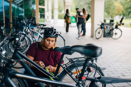Young female student unlocking cycle at parking station in campus