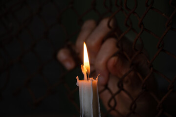 female hands hang on a fence made of iron mesh in the lock on the background of a burning candle