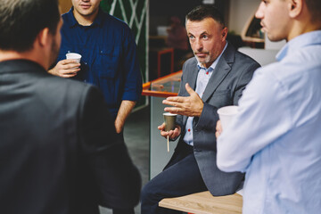 Professional male colleagues have business conversation during coffee break in company office, crew of executive managers in smart casual wear communicating about involved project and analytics