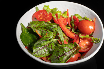 Vegetarian salad of cherry tomatoes, spinach, red onions and bell peppers with butter. On a black background.