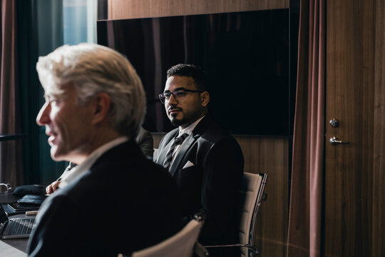 Confident businessman sitting with senior male colleague in board room during meeting