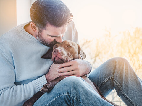 Handsome man and a charming puppy. Close-up, indoors. Studio photo, white color. Concept of care, education, obedience training and raising pets