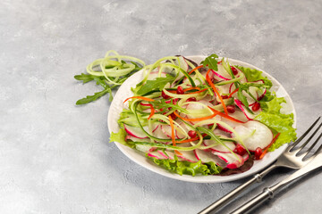 Vegetarian salad of radish, spinach, red onion and bell pepper and cucumber. On a light background.